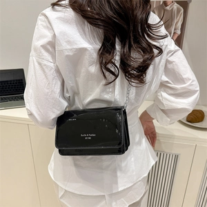 Glossy black patent leather chain crossbody bag shown on a model in a minimalist setting