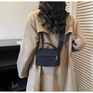 Detailed back view of a black nylon crossbody bag on a model wearing a camel coat