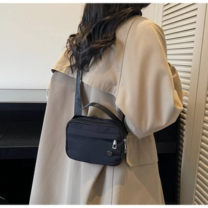 Detail view of a black nylon crossbody bag with adjustable straps worn over a trench coat