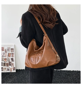 Detail of a large brown soft leather tote bag showing textured geometric embossing and metal hardware