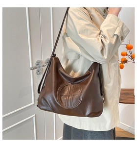 Close-up of deep brown tote bag with embossed logo and wrinkled leather texture