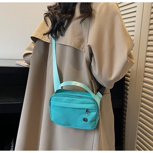 Detail of mint green nylon crossbody bag with adjustable strap worn on khaki trench coat