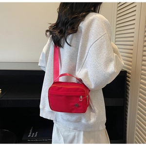 Detail view of red nylon crossbody bag with adjustable strap and circular metal logo