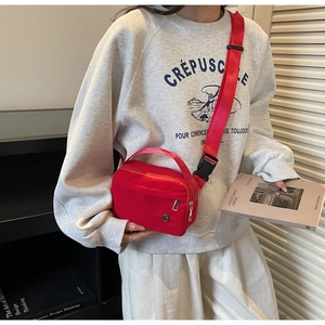 Model wearing a red nylon crossbody bag with adjustable strap and top handle for travel