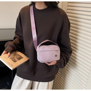 Close-up of a lilac nylon crossbody bag featuring a front zipper and wide strap