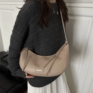 Minimalist beige crescent shoulder bag in smooth faux leather with gold buckle detail