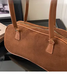 Detail of a brown suede baguette bag featuring smooth metal zipper and slim leather handles