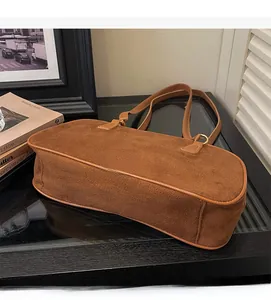 Detailed texture of brown suede baguette bag with slim shoulder straps in a cozy home setting