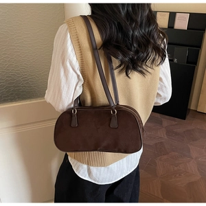 Detail of dark brown suede shoulder bag with thin straps on model in warm interior