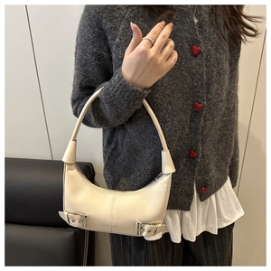 Detail view of cream crescent shoulder bag with silver buckle accents and leather texture