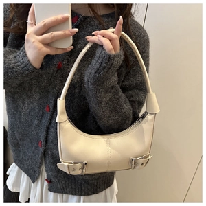 Close-up of cream-colored crescent bag with silver decorative buckles and matte finish