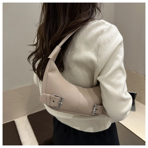 Detail of a beige hobo bag with silver buckle accents worn by a model in a minimalist setting