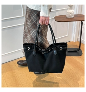 Detail van zwarte shopper tas met zilveren ringdecoratie en leren trekkoord