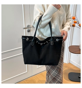 Detail van de minimalistische zwarte shopper met metalen oogjes en een smalle gespband