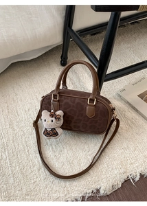Detail of retro leopard print Boston bag with plush cat charm on soft white rug