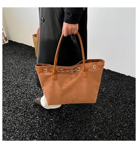 Detail of a large brown suede tote bag with metal buckle held by a model in a minimalist setting