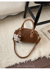 Detailed view of a leopard print bowling bag with leather handles and a plush charm