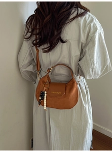 Sac bandoulière marron en cuir mat avec breloque perlée porté sur un trench-coat