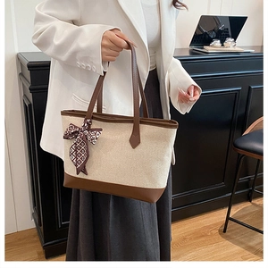 Detail of beige canvas tote with brown leather trim and patterned silk scarf handle