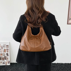 Retro brown leather tote bag with embossed logo worn by model in a minimalist setting