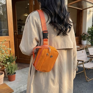 Minimalist bright orange nylon crossbody bag shown worn by a model in a beige coat