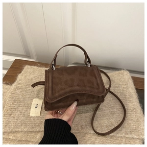 Detail of a mini dark coffee crossbody bag with matte leather texture and retro top handle
