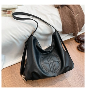 Detail of black lychee texture leather bag with embossed geometric logo and slim strap