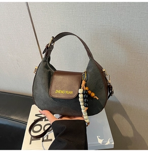Dettaglio borsa a mezzaluna in camoscio grigio con finiture in pelle e perline in legno