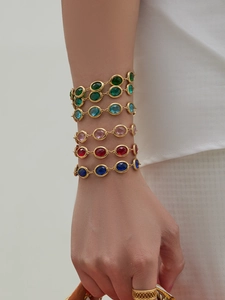 Close-up of a model wearing colorful oval-cut gemstone bracelets with gold-plated finish