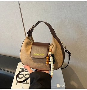 Dettaglio di una borsa a tracolla in pelle marrone e camoscio con un ciondolo con nappa