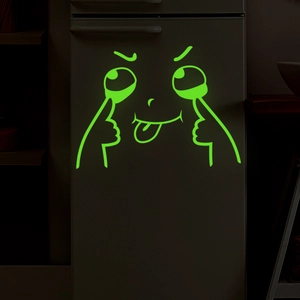 Close-up of luminous green cartoon emoji stickers glowing on a dark refrigerator door