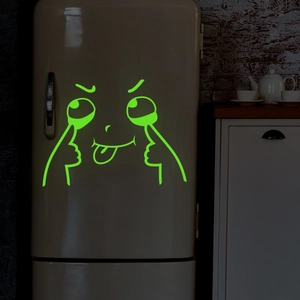Luminous cartoon emoji sticker glowing green on a vintage fridge in a dark room