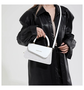 Detail van een witte leren crossbodytas met rond handvat en goudkleurig beletteringslogo