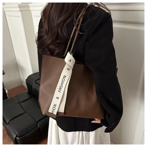 Close-up of brown tote bag side showing white canvas strap with Fashion text detail