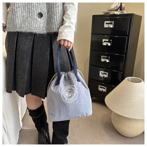 Detail of light blue waterproof bucket bag with drawstring closure and cartoon bear logo