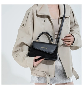 Detalle de bolso de mano minimalista en cuero negro mate con letras doradas y asa delgada
