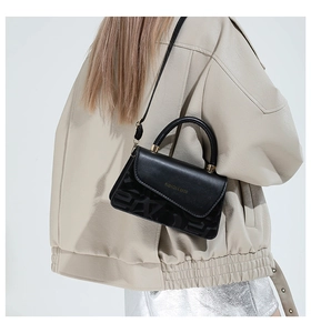 Detalle de bolso bandolera negro con textura grabada y herrajes dorados en modelo