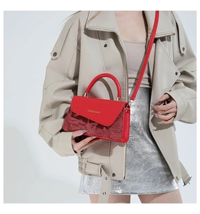 Detalle del bolso cuadrado de cuero rojo con logo dorado y correa ajustable