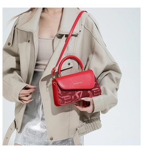 Détail du sac carré rouge avec texture embossée et lettrage doré porté par le mannequin