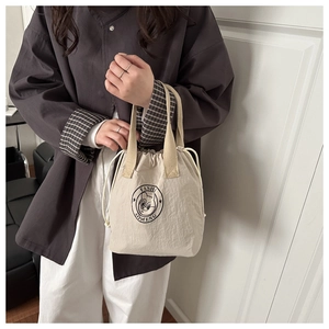 Close-up of beige drawstring bucket bag with black cartoon logo and textile handle