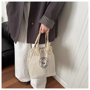 Detailed shot of beige drawstring lunch bag featuring a cartoon cat logo and fabric handle