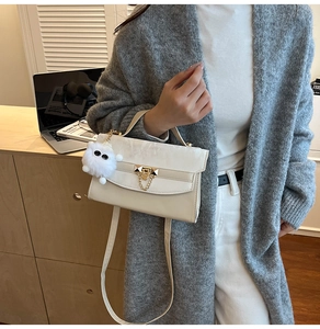 Detail of a creamy white crossbody bag with gold lock and plush charm on a cozy desk