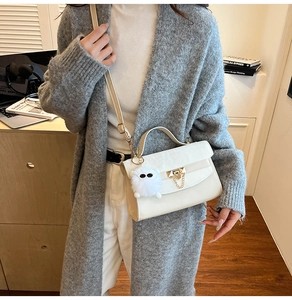 Detail of a beige leather handbag with gold chain, plush charm, and top handle worn by a model