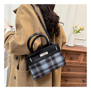 Detail of vintage plaid handbag with metal clasp held by a model in a warm room