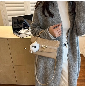 Detail of khaki embossed shoulder bag with plush ball charm on a model in gray cardigan