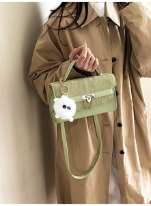 Detail of light green pleated crossbody bag with gold buckle and plush ball accessory