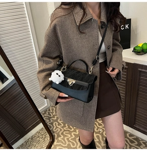 Detail of black matte leather crossbody bag with gold lock and faux fur ball charm