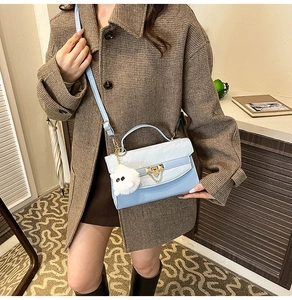 Close-up of a blue structured crossbody bag with gold lock and plush charm on a model