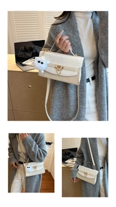 Close-up of beige handbag featuring gold V-buckle, plush charm, and chain detail