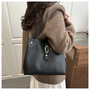 Detail of minimalist black leather tote bag with gold buckle and rivet accents